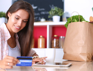 Smiling woman online shopping using tablet and credit card in kitchen