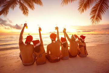 Back view of people with Santa hats sitting on beach