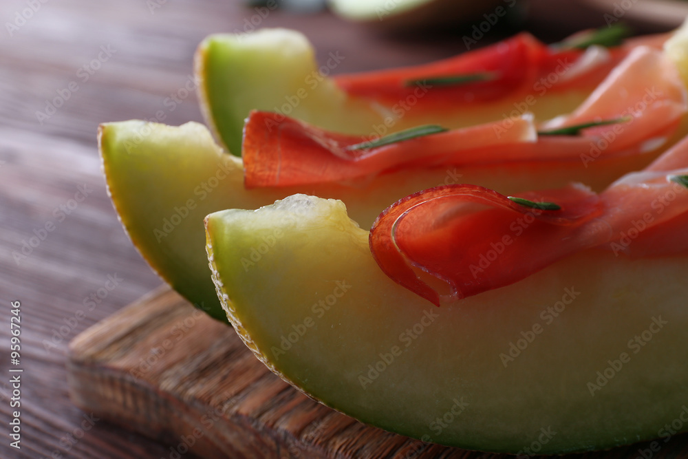 Melon with prosciutto of Parma ham on wooden table, closeup