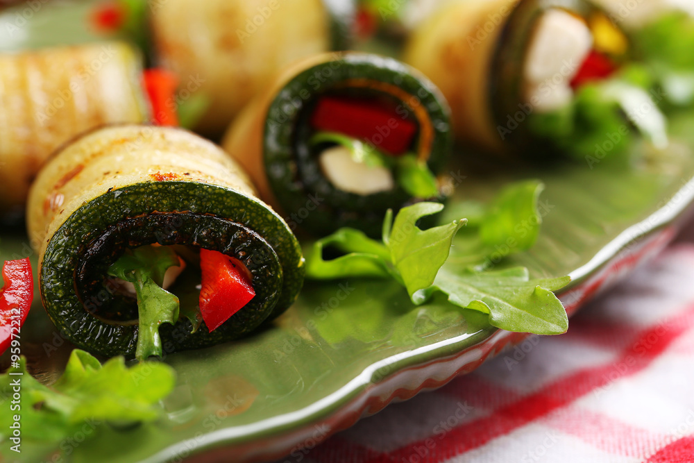 Zucchini rolls with cheese, bell peppers and arugula on plate, close-up