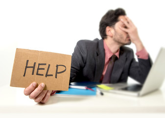 businessman in suit and tie sitting at office desk working on computer laptop asking for help holding cardboard sign