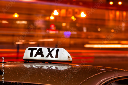 Zdjęcie XXL Błyszczące napisy na napis Taxi przeciwko przejeżdżającym samochodom na ulicy w nocy z dużym cit