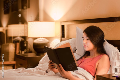 Fotografie, Obraz Biracial teen girl reading book in bed at night