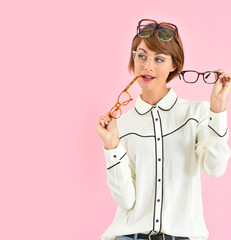 Cheerful trendy girl having trouble choosing eyeglasses