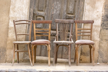 Old and dusty wooden chairs in front a wooden door.