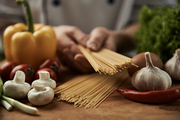 Woman chef cooking italian pasta with garlic,  pepper, mushrooms, tomatoes and greens on wooden table.  