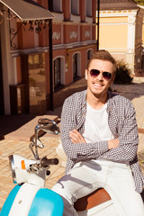 Handsome cute man with glasses sitting on a scooter crossing han