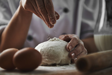 Female in chef uniform adding flour to dough preparing pizza in the kitchen. Cookery and healthy nourishment concept. 