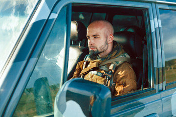 Bald soldier in uniform is driving military vehicle.