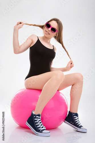 Fototapeta na wymiar Young sportswoman having fun sitting on pink fitball