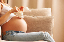 Pregnant Woman At Home Holding Small Baby Shoes