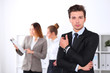 © rogerphoto - Cheerful business man in office with colleagues in the background, sturt  up team