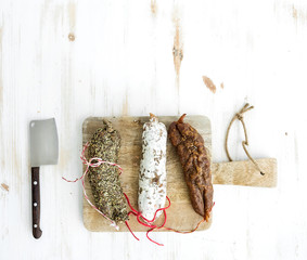 Wall Mural - French alsacian smoked salamis on rustic wooden chopping board over white backdrop, top view