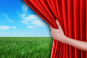 Human hand opens red curtain on field background