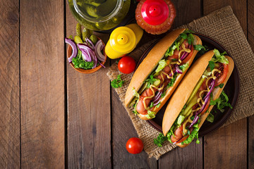 Hot dog with pickles, tomato and lettuce on wooden background