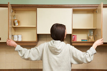 Woman Looking In Empty Food Cupboards
