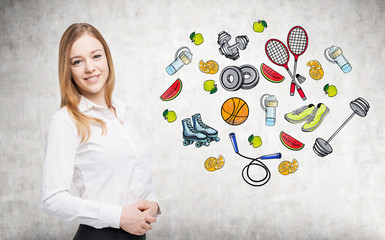 A beautiful lady who is trying to make a choice in favour of a certain sport activity. Colourful sport icons are drawn on the concrete wall. A concept of a healthy lifestyle.