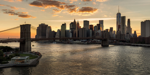 Wall Mural - Lower Manhattan and Financial District skyline at sunset with the Brooklyn Bridge over the East River. Silhouettes of skyscrapers catch the last last of the daylight. New York City
