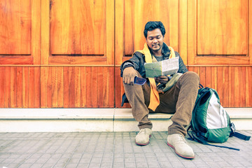 Young indian guy looking city map holding mobile phone - Asian model male next to old wooden door - Cheerful afro american student reading - Concept of tourism DIY and freedom - Soft vintage filter