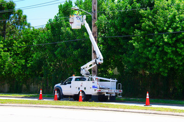 Electrician working on high power lines from a lift on the back of a truck that is parked in the street and surrounded by warning cones