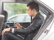 © bokan - Young businessman using mobile phone while sitting on the back seat of the car