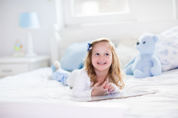 Wall Mural - Little girl playing with toy and reading a book in bed