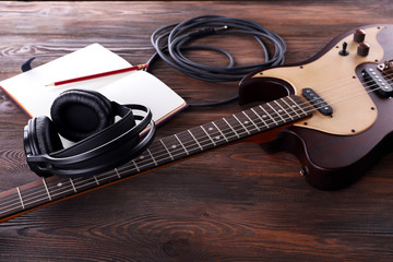 Electric guitar with headphones and notebook on wooden table close up