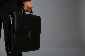 Elegant man in suit with briefcase on gray background