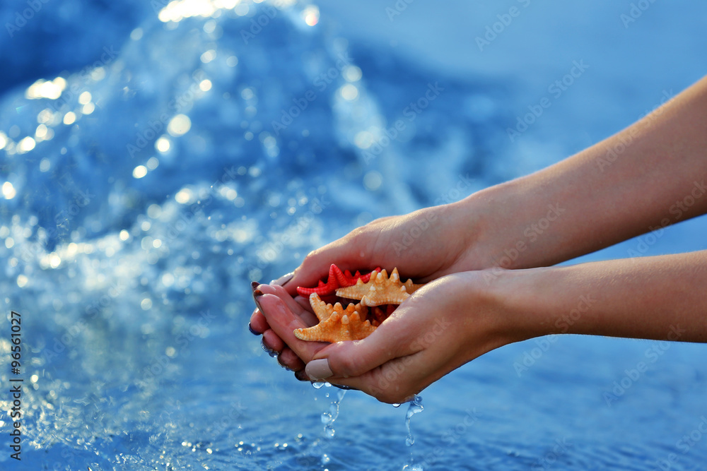 Female hands holding sea stars and touching water