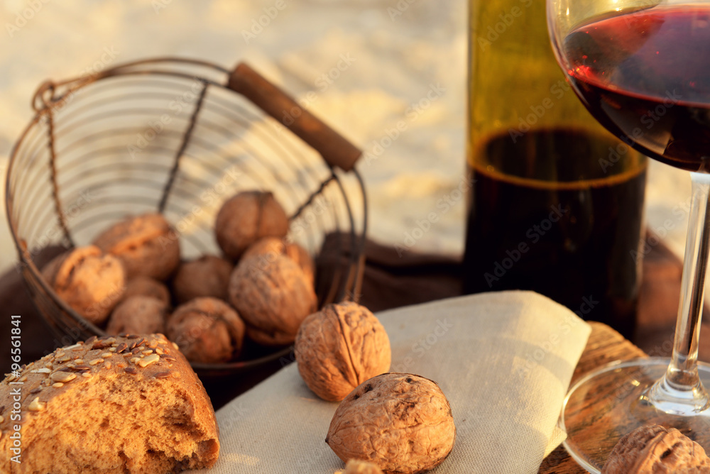 Beautiful romantic composition of red wine, bread and nuts on sandy beach, close up