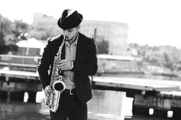 Young man playing on saxophone on the riverside