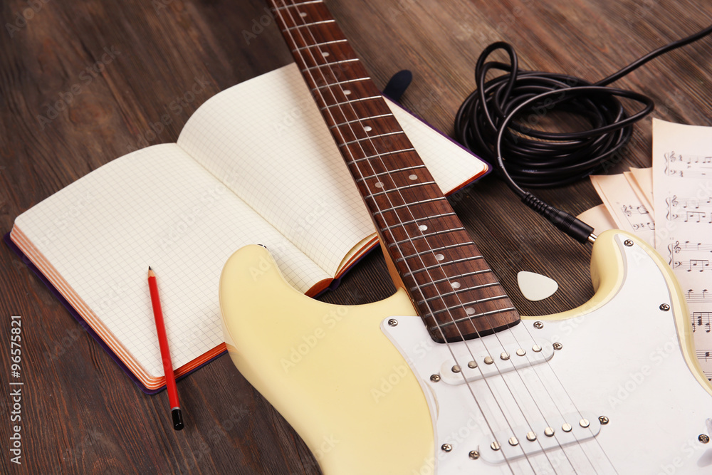 Electric guitar with musical notes and cord on wooden background