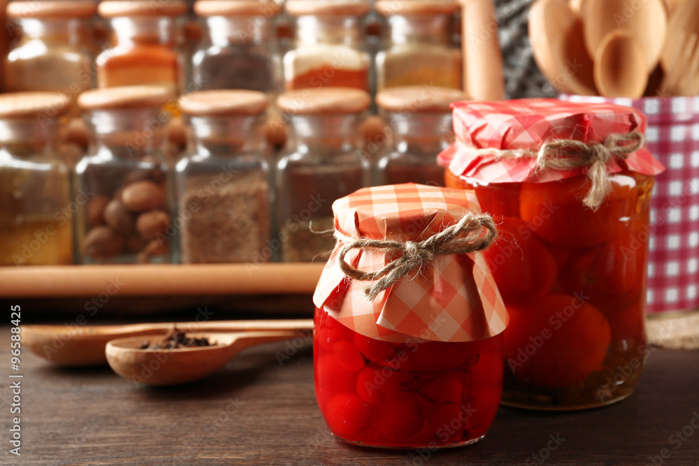 Jars with pickled vegetables and beans, spices and kitchenware on wooden background