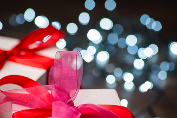 Christmas gift boxes with red bow and lights on wooden surface