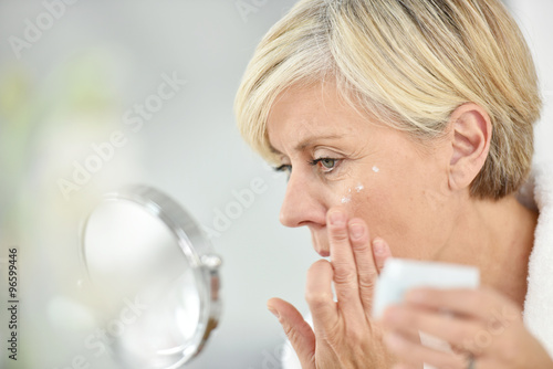 Fotografía Senior woman in bathroom applying anti-aging lotion