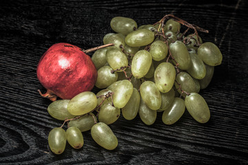 Wall Mural - Ripe fresh juicy grape and pomegranate on a black table or board