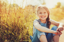 Happy Child Girl In Jeans Overall Playing On Sunny Field