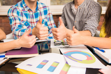 Closeup photo of a young group showing thumbs up working on busi