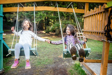 Two Happy Little Girls Swinging On The Swing 