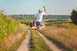 Fototapeta  - Backview of excited man with suitcase jumping on country road