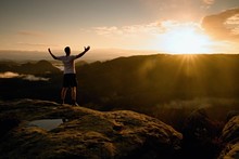 Runner On The Peak. Man In His Target Gesture Triumph With Hands In The Air. Crazy Man In Black Pants And White Cotton T-shirt,