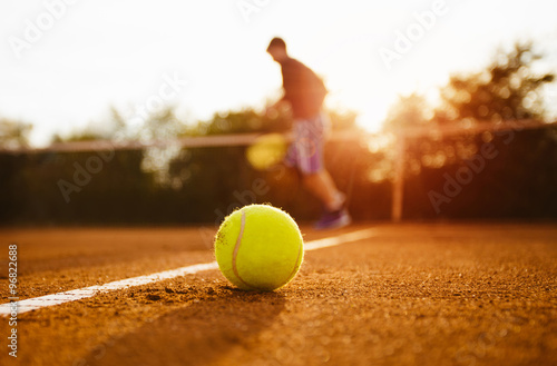 Poster Tennis ball and silhouette of player on a clay court