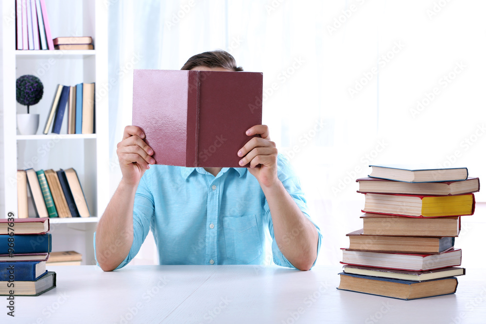 Young man reading book at table in room