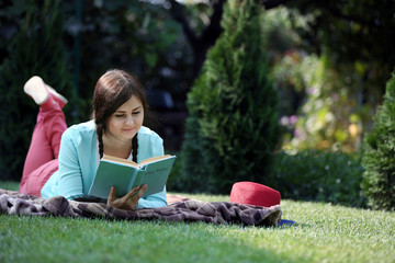 Wall Mural - Young woman with book lying on green grass outdoors