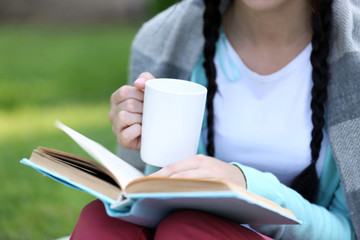 Wall Mural - Young woman with book sitting on green grass outdoors