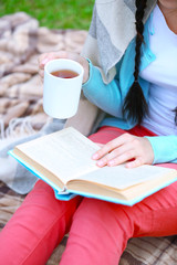 Wall Mural - Young woman with book sitting on green grass outdoors