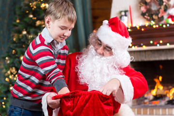 Wall Mural - Santa Claus giving a present from sack to child boy near the fireplace and Christmas tree at home