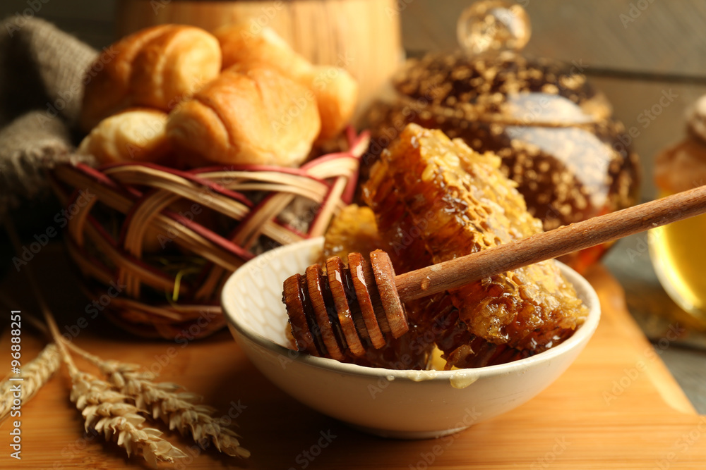 Honeycombs on plate, hot buns in basket on wooden background