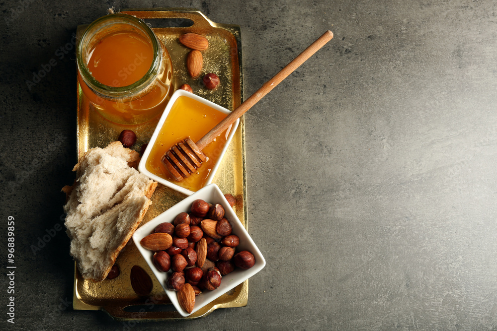 Glass jar and bowl with honey and nuts on gray background
