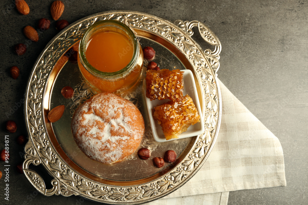 Glass jar and bowl with honey and nuts on gray background